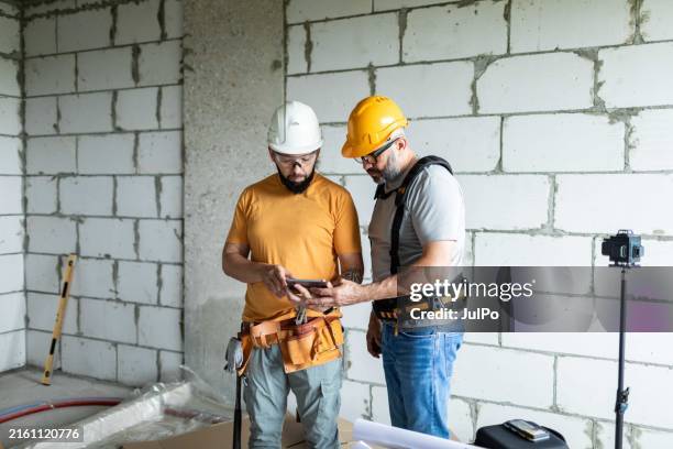 front view of two construction workers analyzing blueprints using digital tablet at construction site - overalls stock pictures, royalty-free photos & images