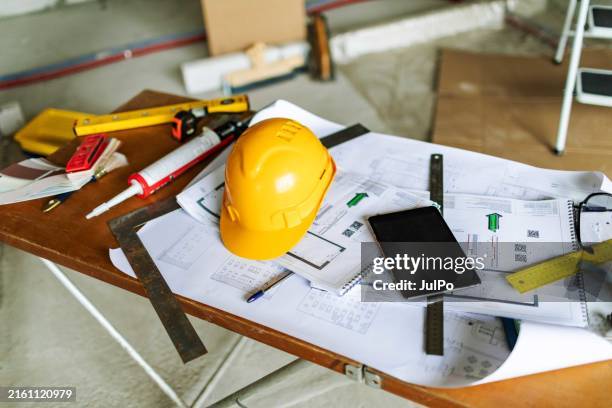plans architecturaux, casque de sécurité et outils de travail sur la table sur le chantier de construction - équipement de construction photos et images de collection
