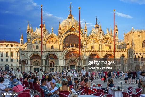Basilica San Marco reflected in acqua alta in Piazza San Marco at twilight during sunset, Venice, Italy with motion blur on the crowds of tourists.