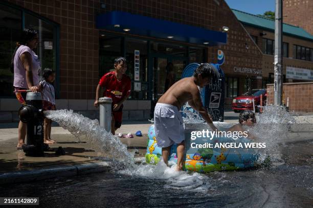 Children cool off with water from an open fire hydrant during a summer heat wave in the Bronx borough of New York on July 11, 2024. As New York and...