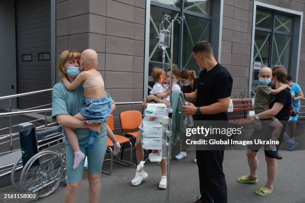 Women hold in arms children, hospital patients, outside the building of one of the largest children’s hospitals of Ukraine, ‘Okhmatdyt’, partially...