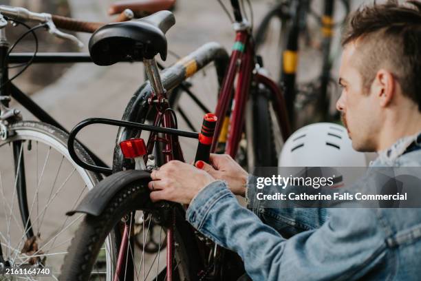 a man secures his bike to a bike rack, using a strong bicycle security device and a padlock with keys - fahrradschloss stock-fotos und bilder