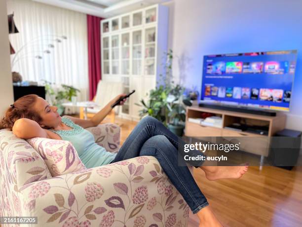 la mujer usa el control remoto para la televisión en la sala de estar - smart tv fotografías e imágenes de stock
