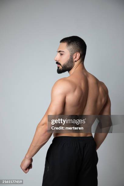 rear view of a muscular man flexing his biceps and showing off his defined back muscles, emphasizing strength and fitness. - posterior view of arm muscles stock pictures, royalty-free photos & images