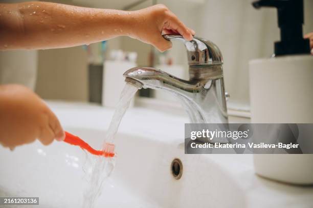 child wets a toothbrush under the tap. - toothbrush stock pictures, royalty-free photos & images