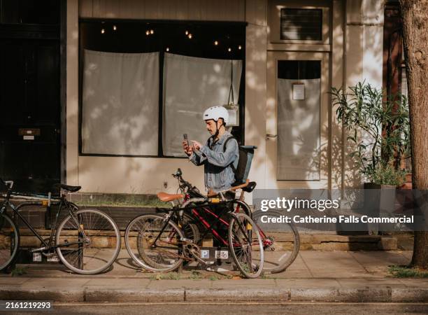 a cyclist uses his phone beside a bike - fahrradschloss stock-fotos und bilder