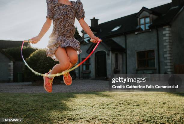a child plays with a jump rope in a garden outside a house on a summers evening - child skipping stock pictures, royalty-free photos & images