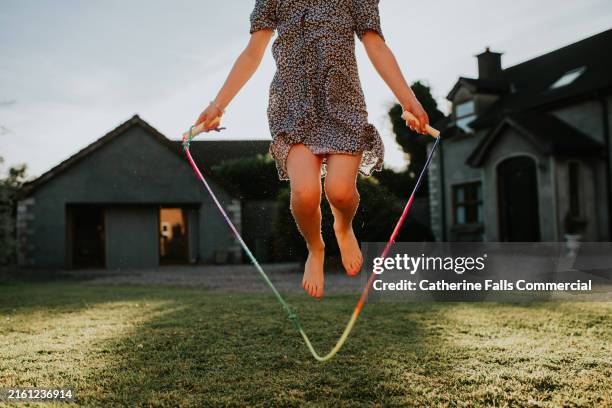 a child plays with a jump rope in a garden outside a house on a summers evening - home insurance stock pictures, royalty-free photos & images