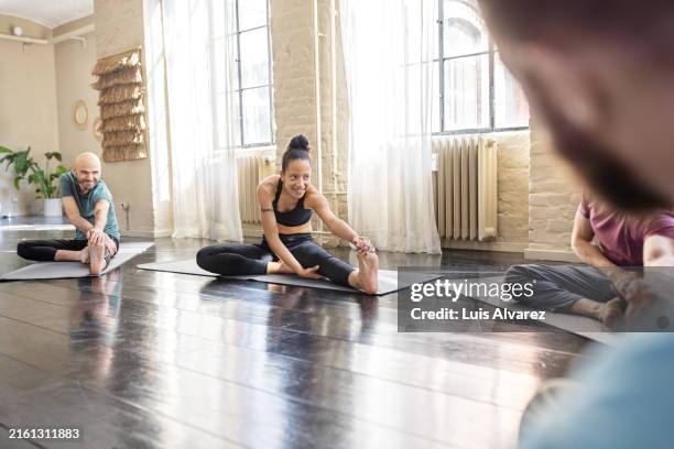 young woman doing stretching workout at yoga class - tapis de sol photos et images de collection