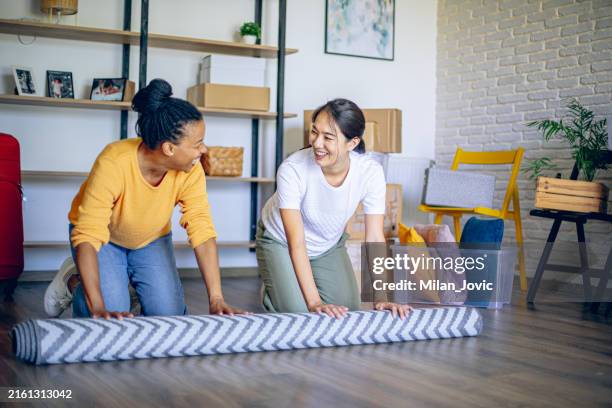 unrolling carpet in new house - black and asian lesbian stock pictures, royalty-free photos & images