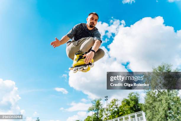 mid-air maneuvers and jumps: man on rollers catching the air against blue sky - skaten stockfoto's en -beelden