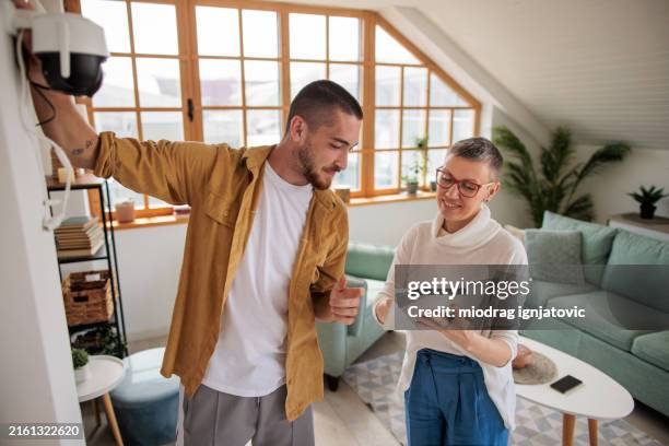 young man and woman installing a home surveillance camera at home - bewakingscamera stockfoto's en -beelden