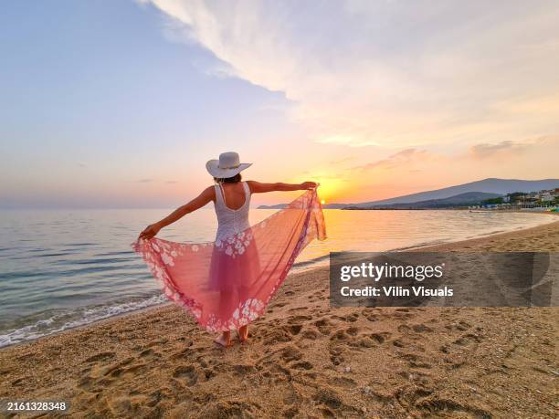 a woman enjoys the sunset on the sea, stretching her arms and holding a scarf - shawl stock pictures, royalty-free photos & images