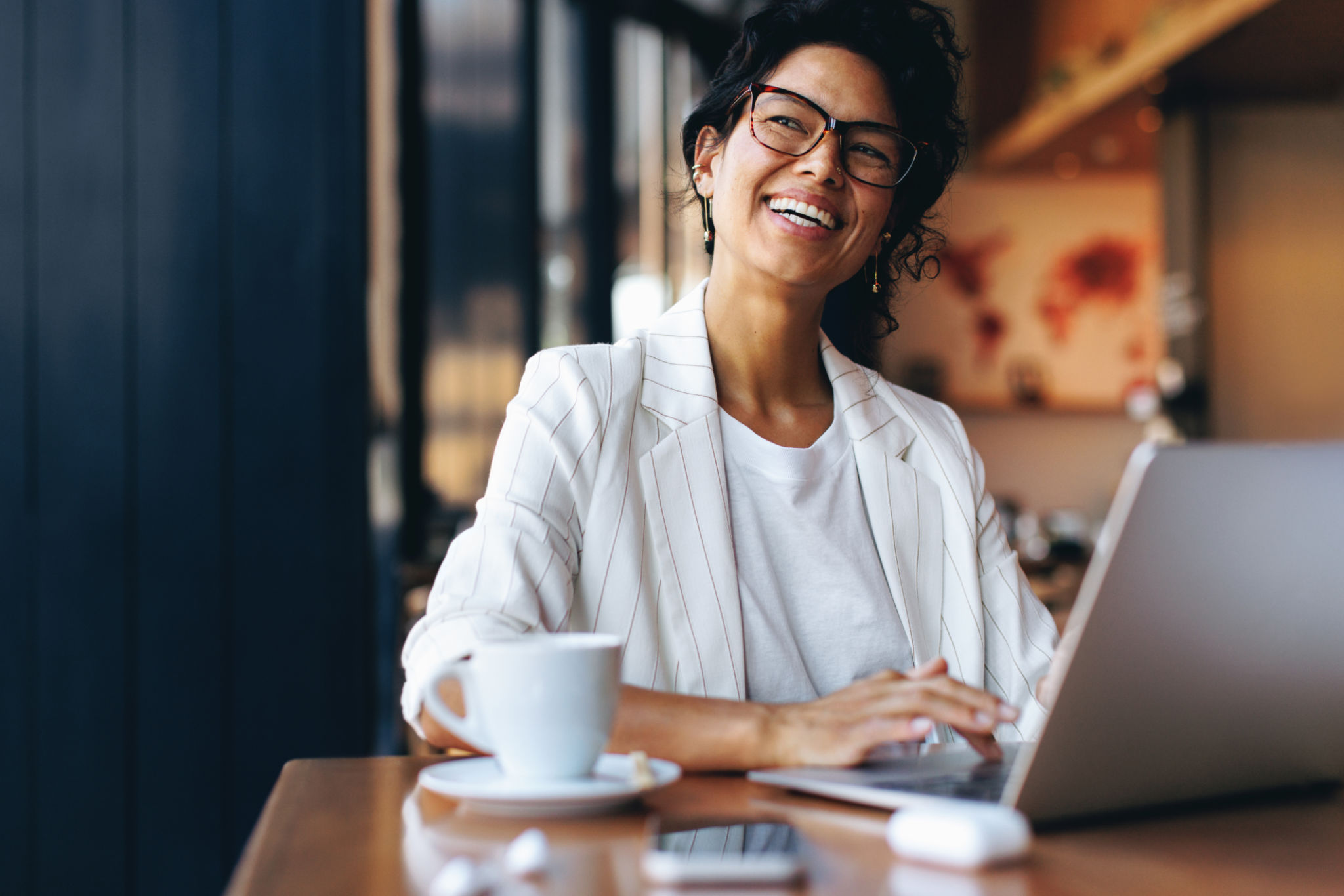 Happy businesswoman working remotely on laptop in a cozy cafe Happy businesswoman working remotely on laptop in a cozy cafe