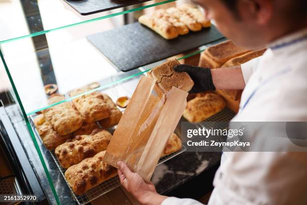 the baker is putting the bread into a paper bag. - pão de leite imagens e fotografias de stock