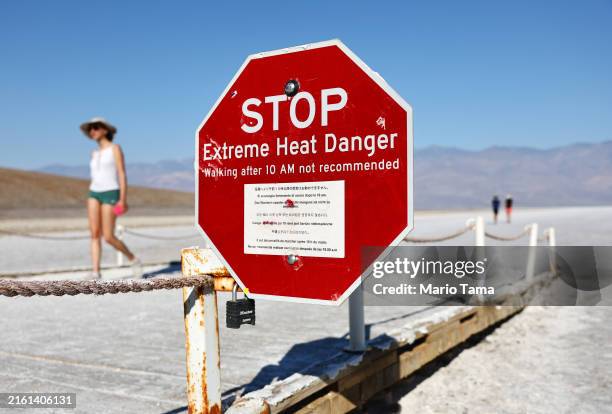 Visitors walk near a 'Stop Extreme Heat Danger' sign in Badwater Basin salt flats in the morning, when temperatures are less hot, during a...