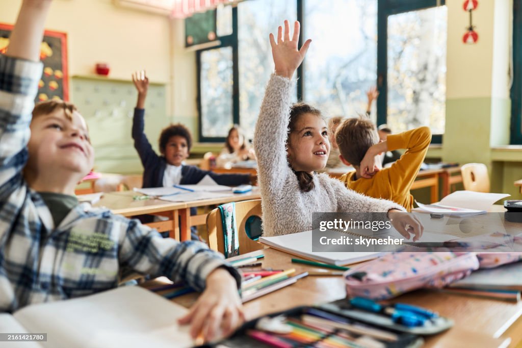Happy schoolgirl and her friends raising hands on a class.