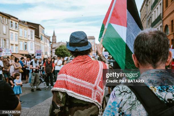 Protester from behind with a red keffiyeh holds a Palestinian flag during a demonstration in support of the people of Gaza and against Israeli...