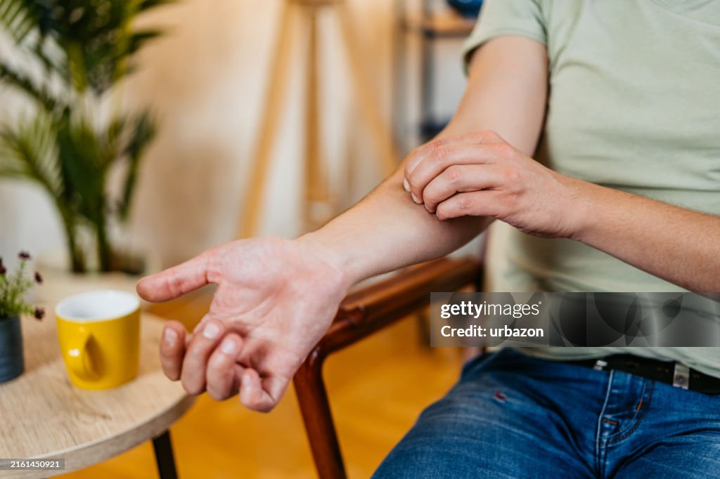 Mid-Adult Man Scratching His Skin While Sitting In An Armchair At Home