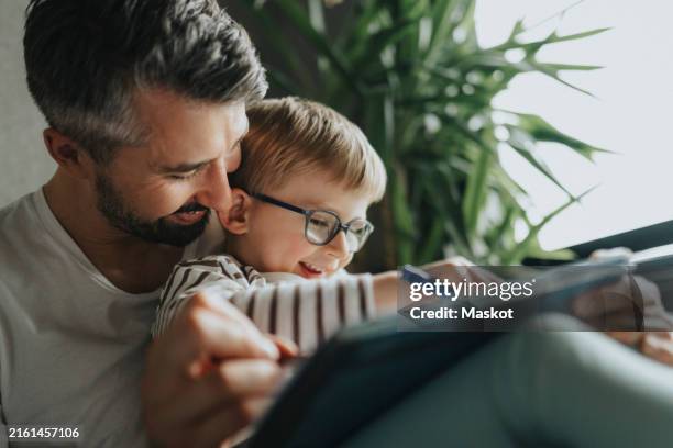 son enjoying leisure time with father while using digital tablet at home - lunettes de vue photos et images de collection