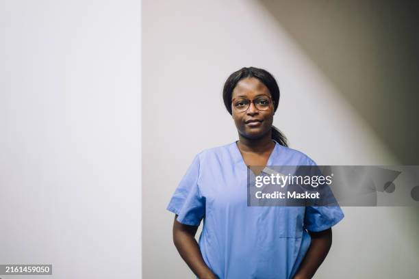 portrait of confident female medical practitioner standing against white wall in hospital - doctor of the arts stock pictures, royalty-free photos & images