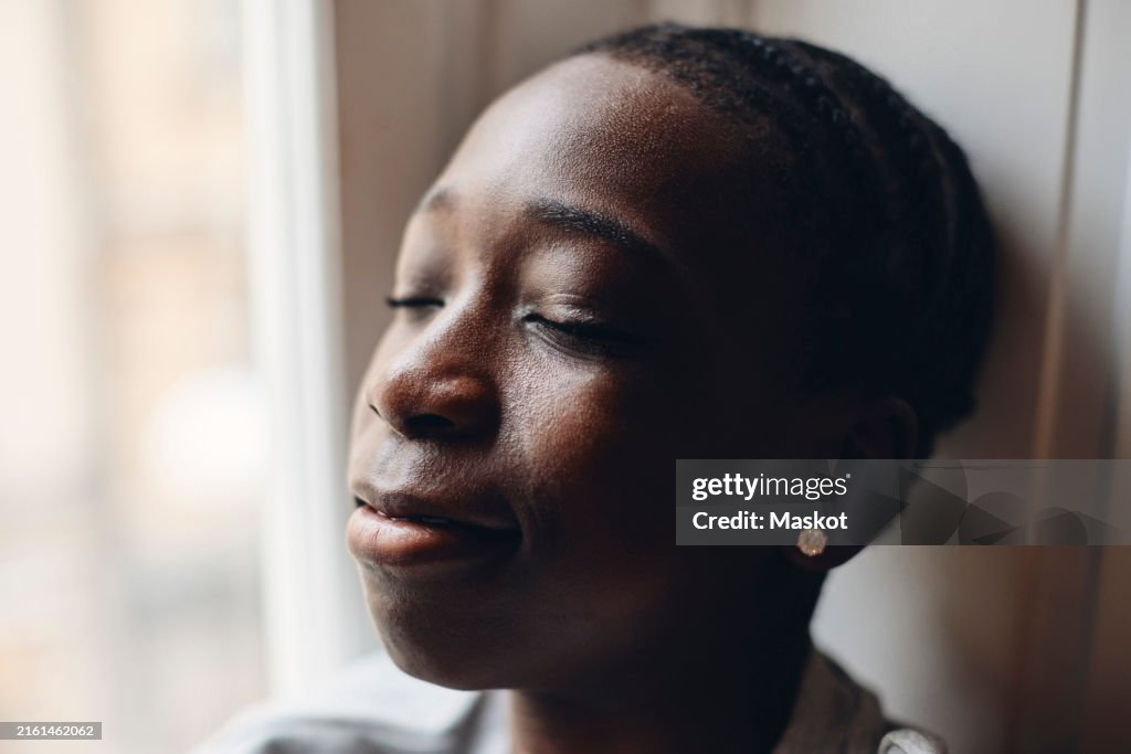 Close-up of teenage boy with eyes closed near window at home