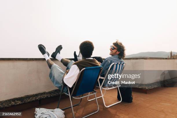 happy male friends spending leisure time while sitting on chairs at rooftop - freund stock-fotos und bilder