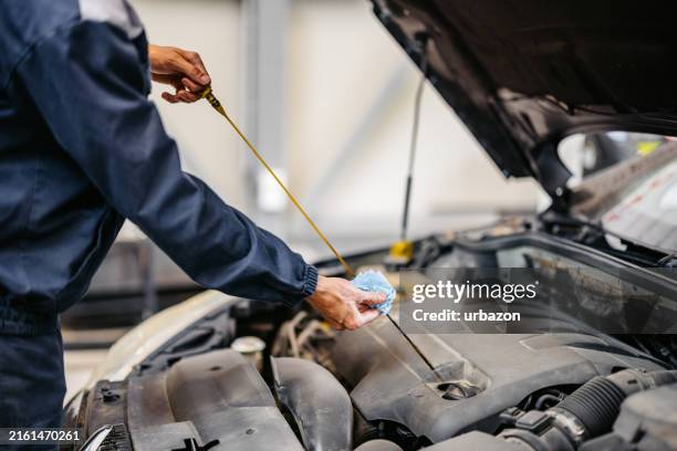 junger automechaniker, der ein motoröl an einem auto überprüft, an dem er in seiner garage arbeitet - ölwechsel stock-fotos und bilder