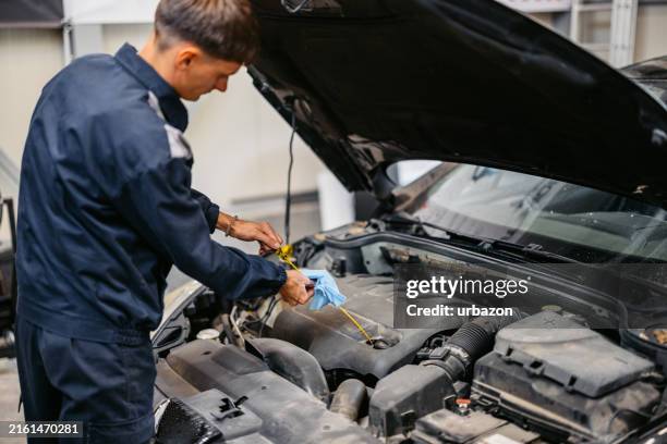 junger automechaniker, der ein motoröl an einem auto überprüft, an dem er in seiner garage arbeitet - ölwechsel stock-fotos und bilder