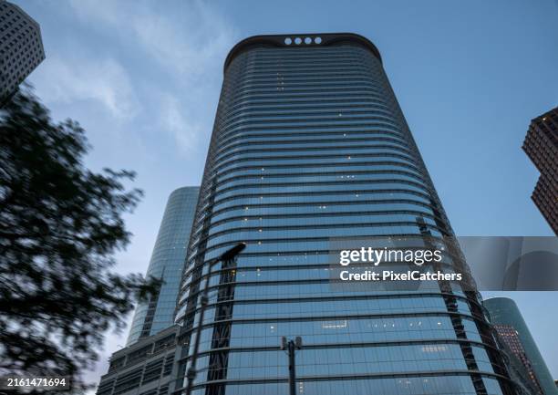 looking up at a modern glass skyscraper with trees in the foreground - postmodern stock pictures, royalty-free photos & images