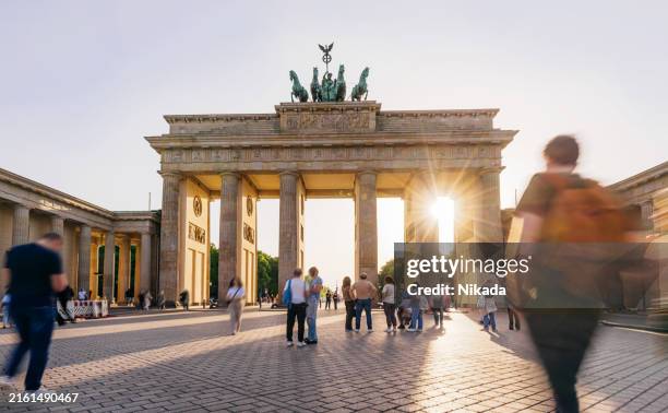 sunset glow at brandenburg gate in berlin, tourists walking - porta de brandemburgo imagens e fotografias de stock