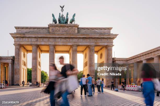 sunset glow at brandenburg gate in berlin, tourists walking - unter den linden stock-fotos und bilder