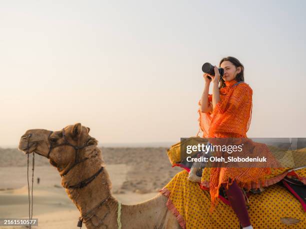 woman photographing with camera while riding camel in the desert at sunset - kamel bildbanksfoton och bilder