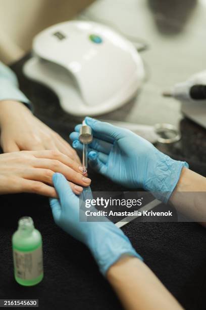 manicure master applying cuticle oil onto female fingernails on nail salon. - uv light manicure stock pictures, royalty-free photos & images