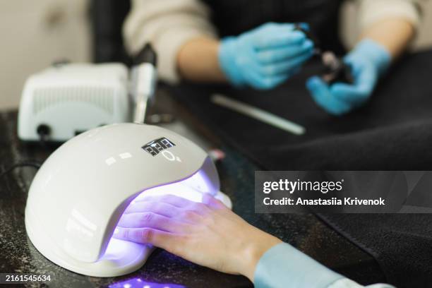 manicurist master is covering painting client's nails and drying it in uv lamp. - gel nail polish stock pictures, royalty-free photos & images