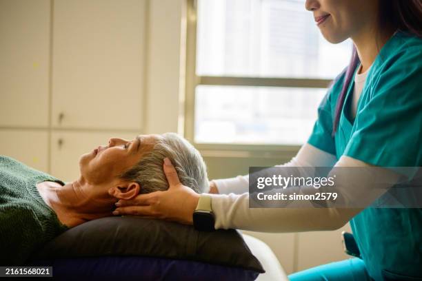 junge asiatische osteopathin, die in einem rehabilitationszentrum eine craniosacral-massage an ihrer älteren patientin durchführt - zentralnervensystem stock-fotos und bilder