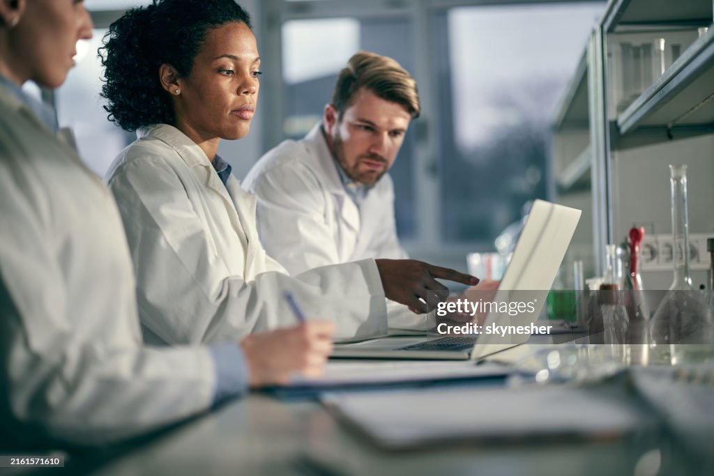 Team of young scientists working on a computer in laboratory.