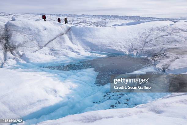 Methane Spring Scientists walk over ice past a river of meltwater as they leave the ...
