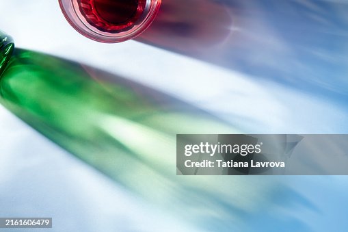 Red and green glass bottles casting beautiful shadows on white background. Top view, flat lay. Red and green glass bottles casting beautiful shadows on white background. Top view, flat lay.
