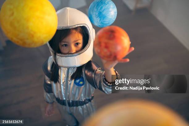 ragazza in una tuta spaziale che gioca a casa, esplorando e imparando a conoscere i pianeti, immaginando i viaggi nello spazio. - astronauta foto e immagini stock