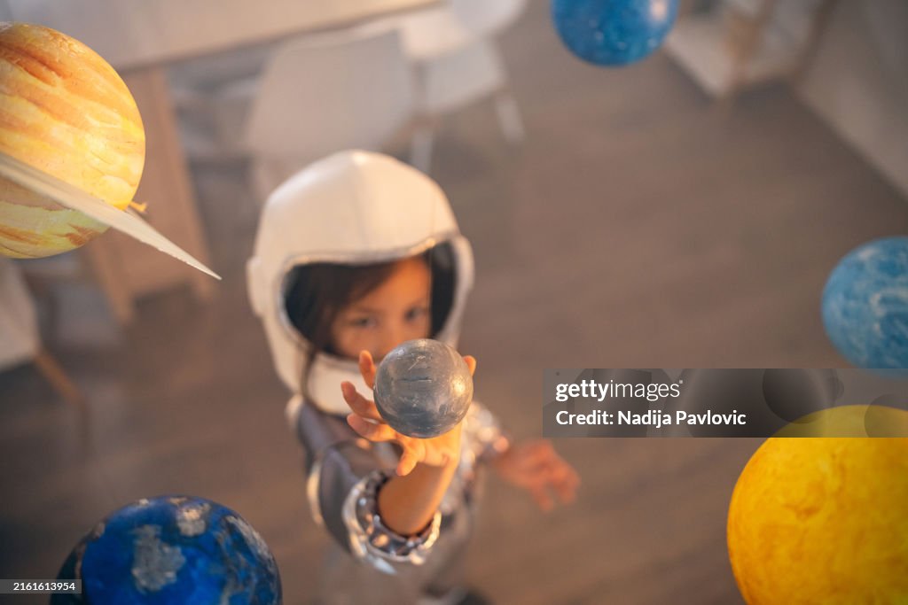 Girl in a space suit playing at home, exploring and learning about planets, imagining space travel.
