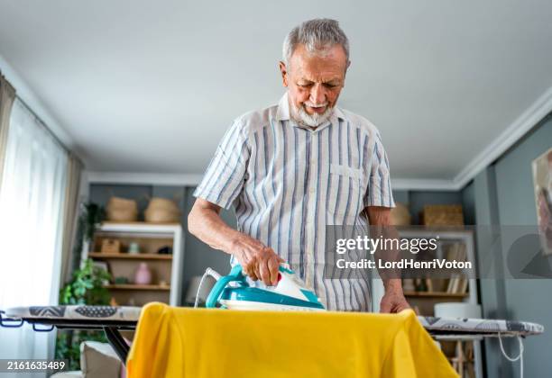 senior man ironing clothes on an ironing board - chores stock pictures, royalty-free photos & images
