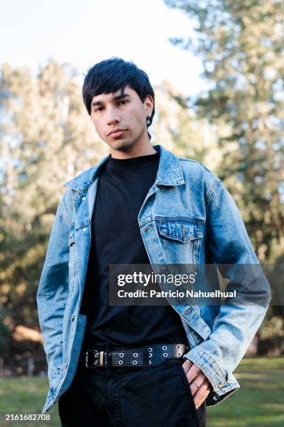 young latino man in denim jacket posing confidently in a forest setting - latino male looking at camera stock pictures, royalty-free photos & images