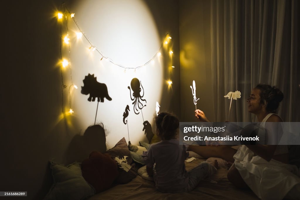 Cute smiling girl with mother playing with shadow puppets.