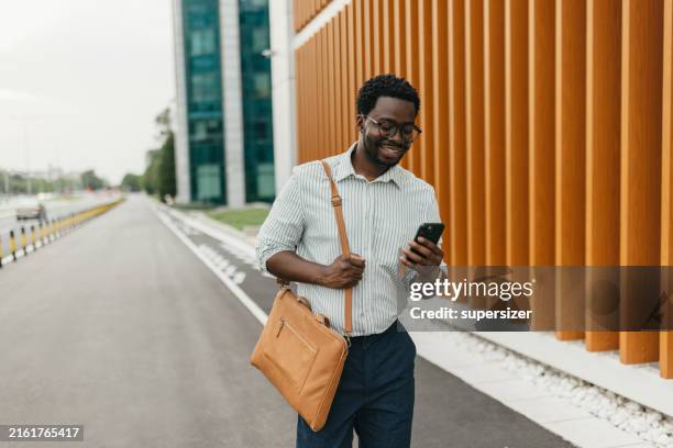 man smiling at his phone while walking down the street. - smart casual stock pictures, royalty-free photos & images