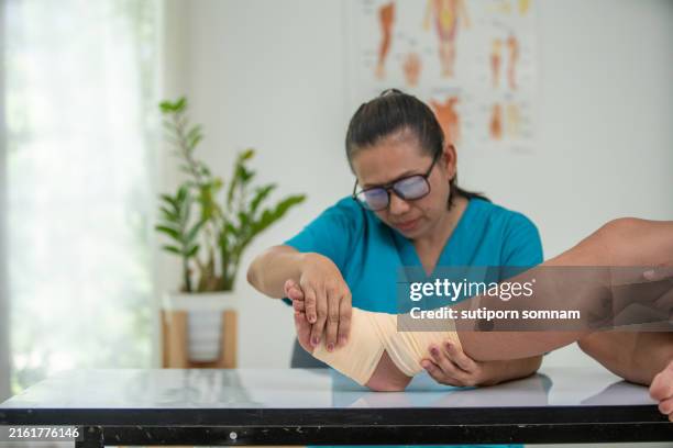a woman nurse in a blue shirt is wrapping a bandage around a man's foot - bandage stock pictures, royalty-free photos & images