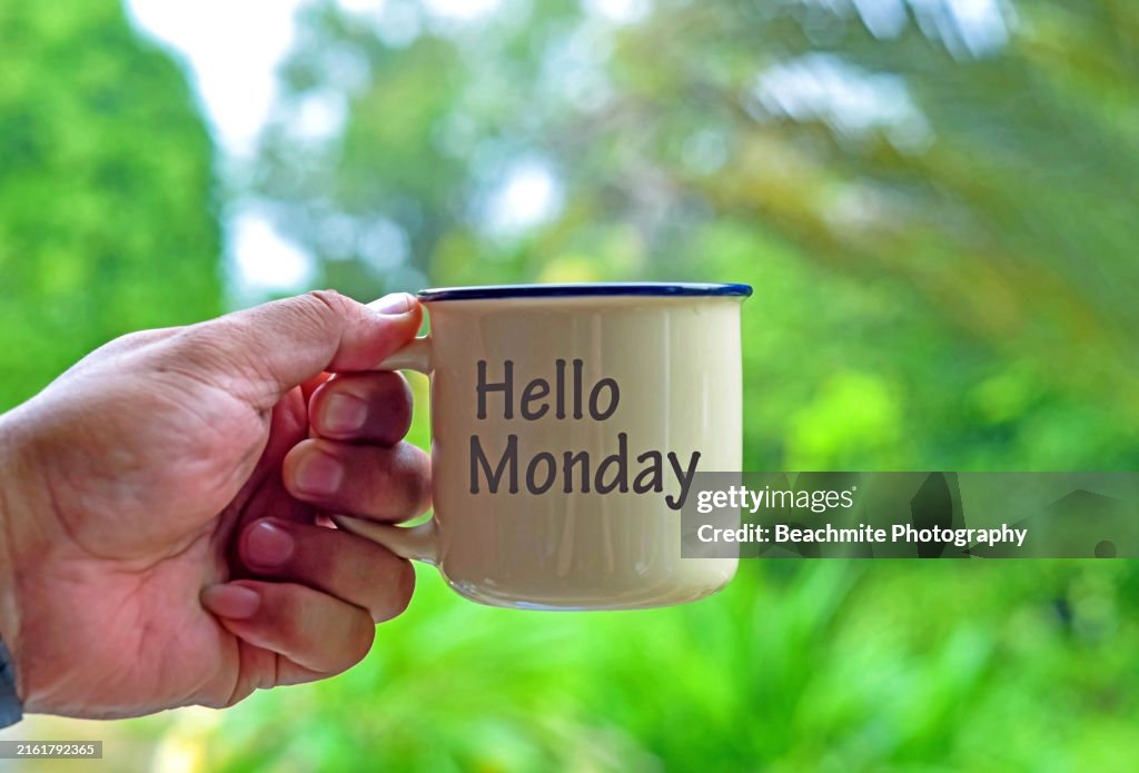 A male hand holding a coffee cup with Hello Monday on green background
