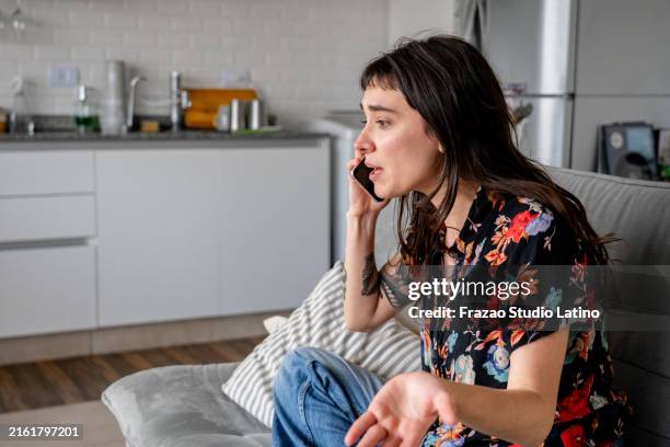 angry young woman talking on mobile phone at home - irritatie stockfoto's en -beelden