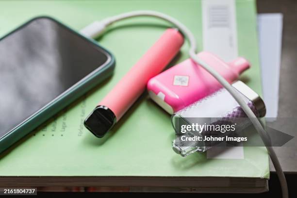 close-up of electronic cigarettes on book beside charging mobile phone - cigarette électronique photos et images de collection