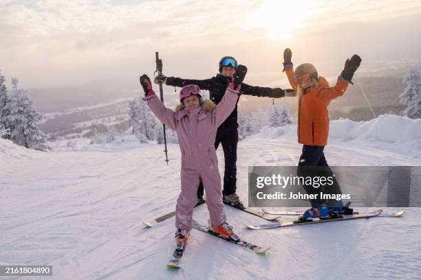 mother and daughters with arms outstretched skiing at sunset - family skiing stock pictures, royalty-free photos & images